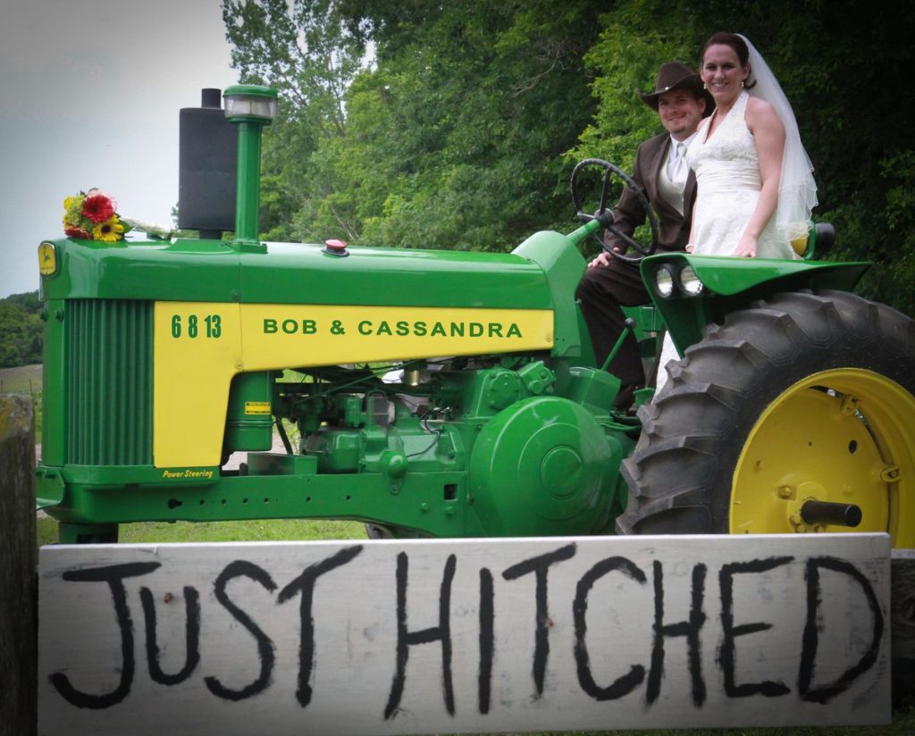newlyweds on 1958 John Deere 530 vintage tractor with Just Hitched sign at country wedding
