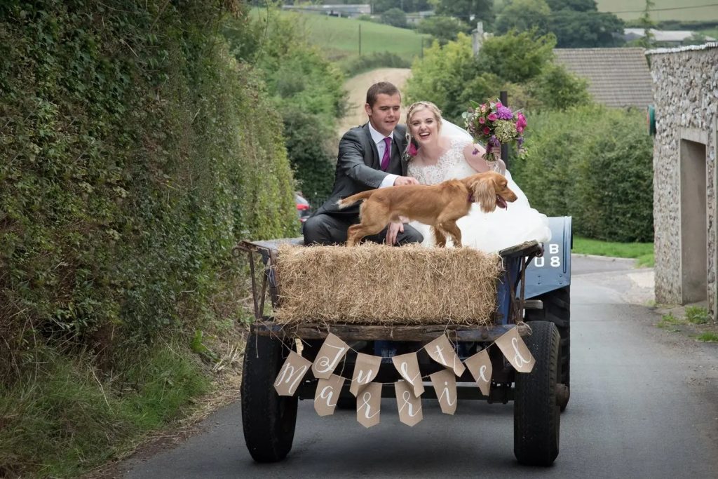 bride and groom on hay wagon pulled by vintage tractor with Just Married banner and dog